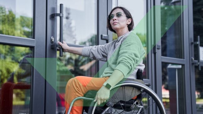 A female wheelchair user is holding a door handle and looking off into the distance before opening the swing door with VAC Green tick